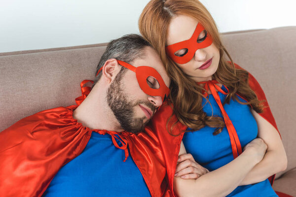 couple of superheroes in masks and cloaks sleeping together on couch 