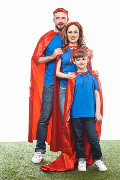 happy family in masks and cloaks standing on lawn and smiling at camera on white