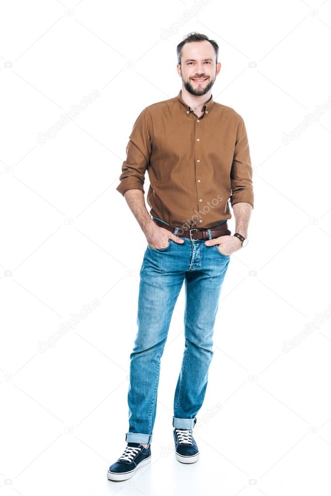 full length view of handsome bearded man standing with hands in pockets and smiling at camera isolated on white