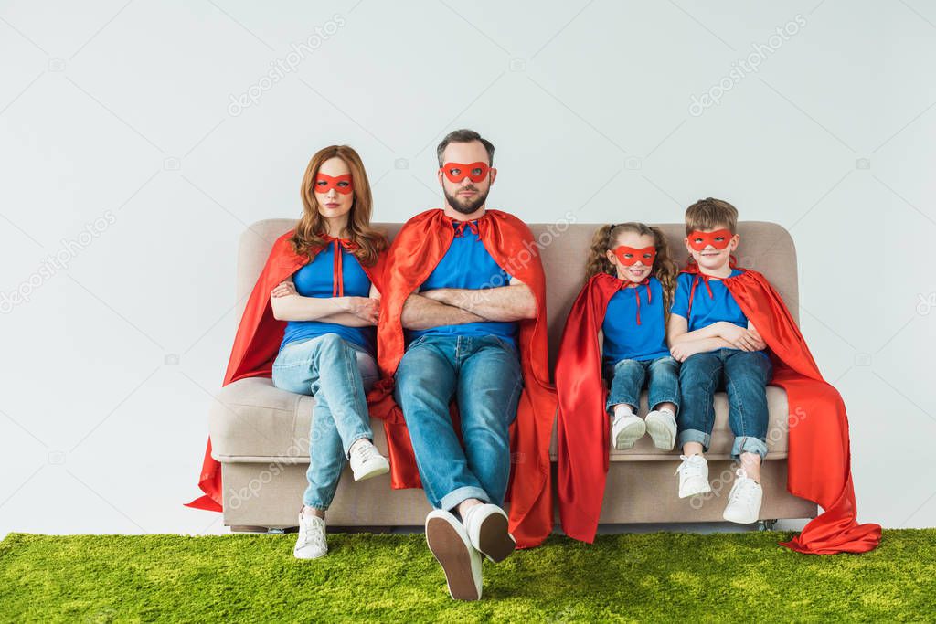 family in superhero costumes sitting with crossed arms and looking at camera on grey 