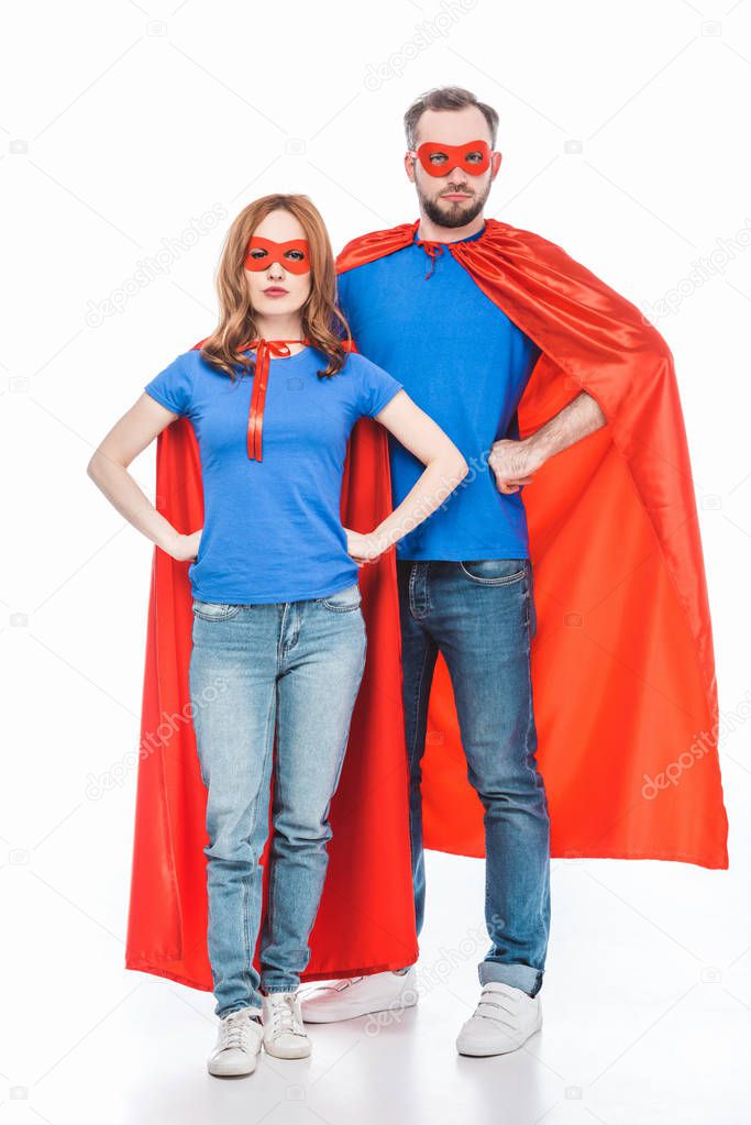super couple in masks and cloaks standing with hands on waist and looking at camera isolated on white