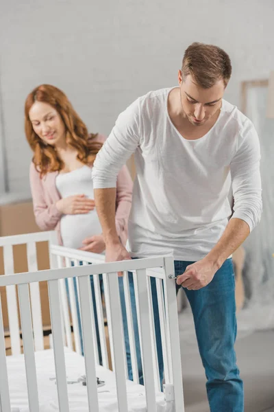 Pregnant Woman Looking Husband Fixing Baby Bed New Home — Stock Photo, Image