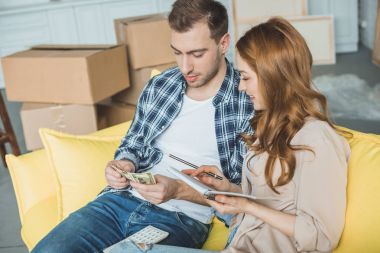 young couple taking notes and counting money while moving home clipart