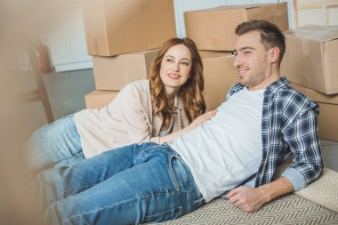 happy young couple looking away while packing boxes and moving home clipart