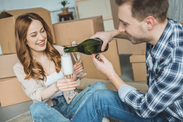 happy young couple celebrating relocation with champagne in new home