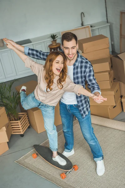 Pareja Joven Divirtiéndose Con Monopatín Nuevo Apartamento Con Cajas Cartón — Foto de Stock