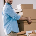 Bearded businessman holding cardboard boxes and looking at camera while moving in new office