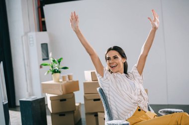 excited young businesswoman raising hands and looking away in new office clipart