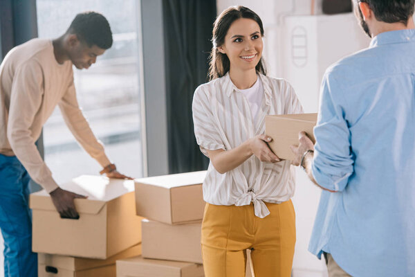 multiethnic coworkers carrying cardboard boxes during relocation in new office  