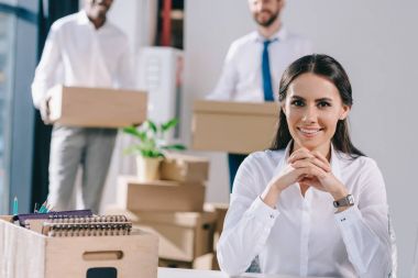 oturma ve kamera kutuları arkasında yeni ofisinde tutan erkek meslektaşları süre gülümseyen genç iş kadını