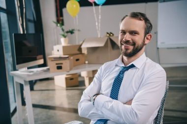 Yeni office balonlarla süslenmiş kamerada gülümseyen çapraz kollu yakışıklı işadamı