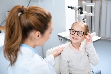 ophthalmologist and smiling kid in eyeglasses in optics  clipart