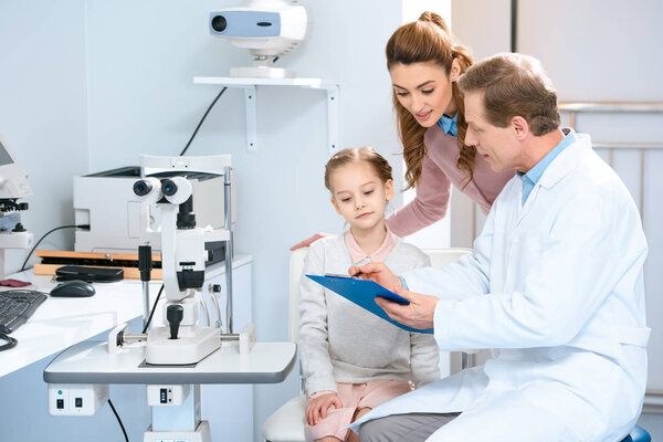 mother and daughter looking at clipboard in ophthalmologist consulting room