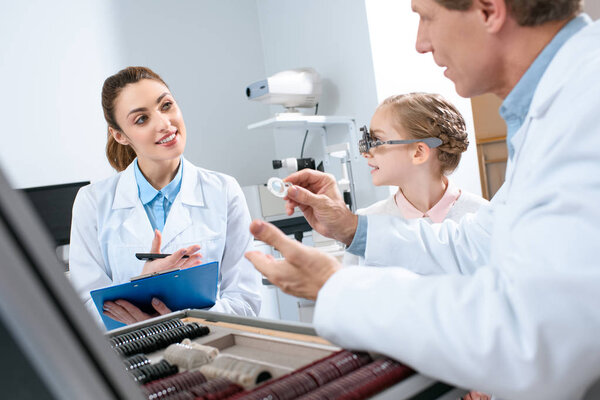 optometrists examining child eyes with trial frame and writing diagnosis