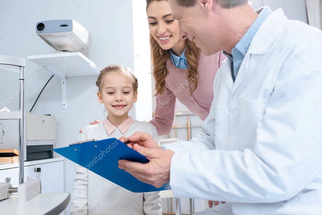 smiling mother and daughter looking at clipboard in ophthalmologist consulting room