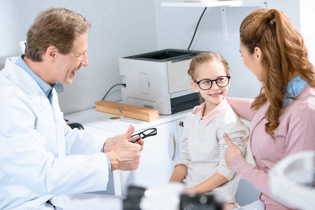 mother looking at daughter with new glasses in oculist consulting room