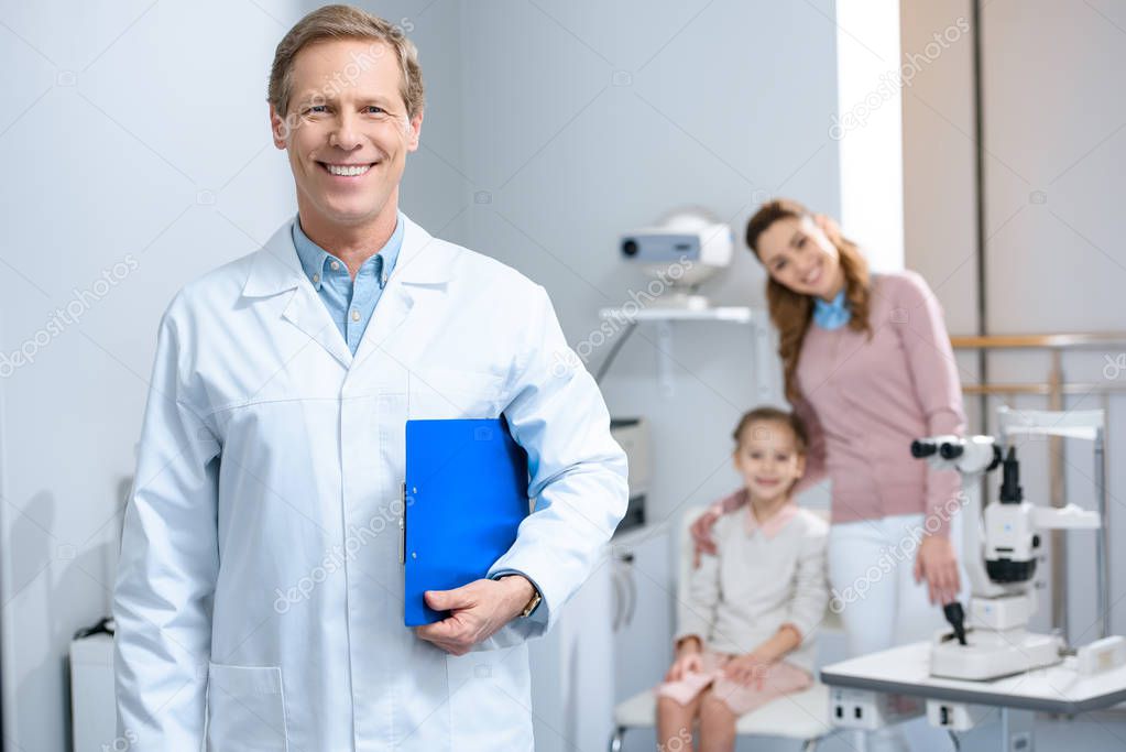 smiling handsome ophthalmologist looking at camera in consulting room