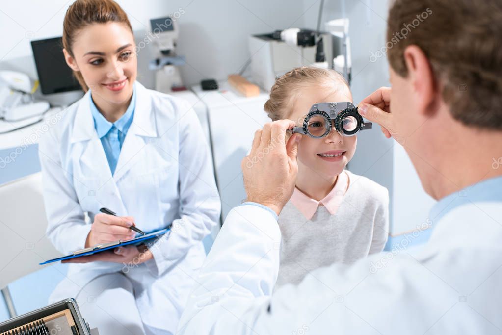 ophthalmologists examining kid eyes with trial frame and writing diagnosis
