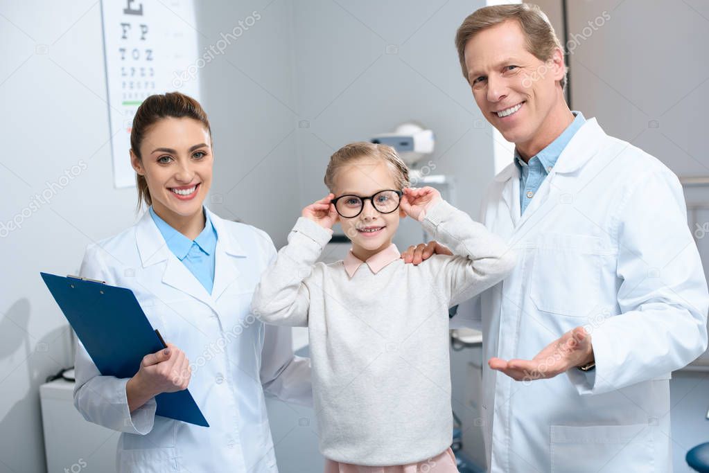 two smiling ophthalmologists and little child in eyeglasses