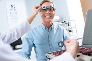 ophthalmologist examining middle aged man eyes with trial frame and lenses clipart