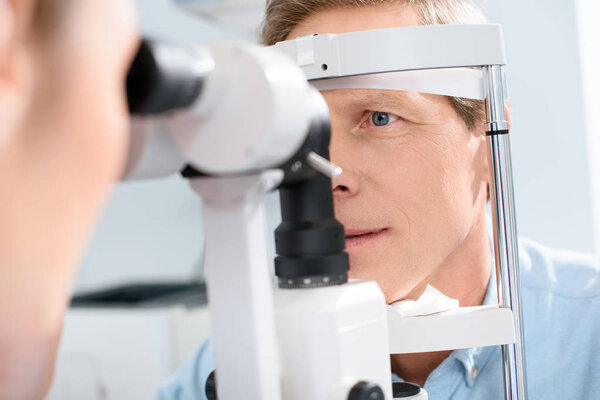 optometrist examining man with modern optical equipment