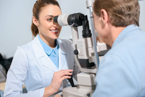 professional optician examining man with modern optical equipment