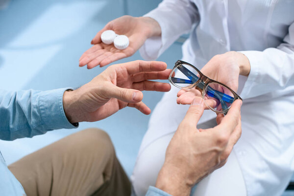 cropped view of man choosing eyeglasses or contact lenses in optical clinic