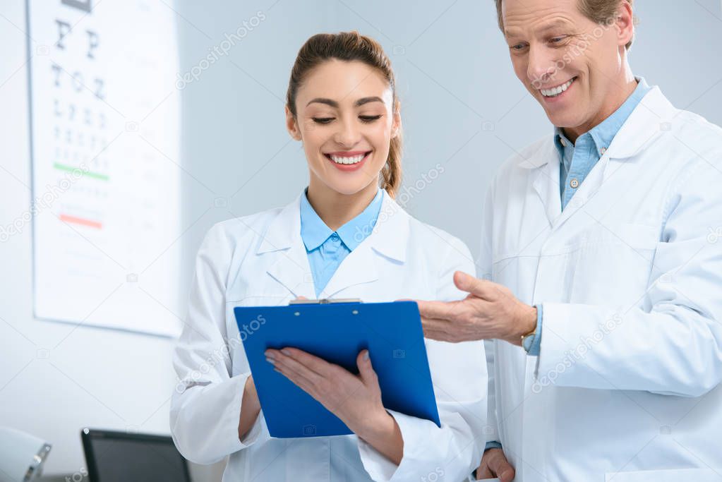 smiling oculists writing diagnosis in clinic 
