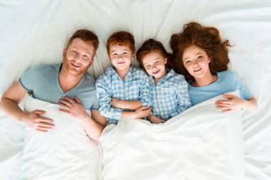 happy redhead family in pajamas lying in bed and smiling at camera  clipart