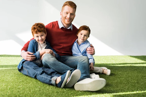 快乐的红头发的父亲和孩子们坐在草地上 微笑着在灰色的相机 — 图库照片
