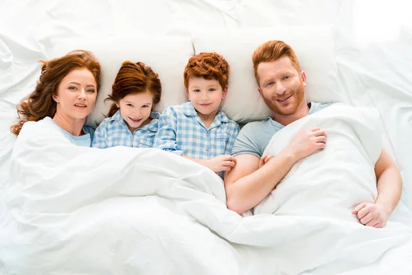 パジャマを着てベッドに横たわって カメラで笑顔の幸せな家族 — ストック写真