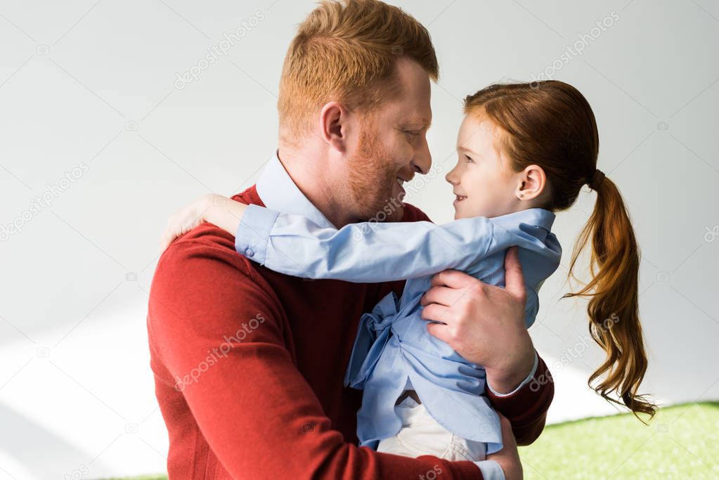 happy redhead father and daughter hugging and smiling each other on grey