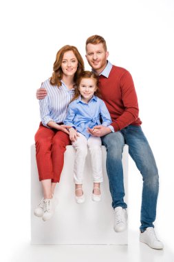Beyaz küp üzerinde oturan ve üzerinde beyaz izole kamera gülümseyen mutlu Kızıl saçlı aile