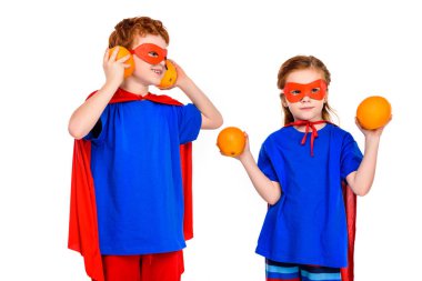 cute super children in masks and cloaks holding oranges isolated on white clipart
