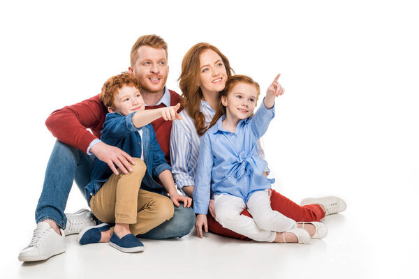 smiling family with two kids pointing away with fingers isolated on white