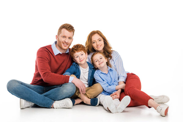 Счастливая рыжеволосая семья с двумя детьми, сидящими вместе и улыбающимися перед камерой на белом фоне
