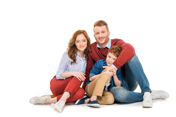 happy parents with cute little son sitting together and smiling at camera isolated on white