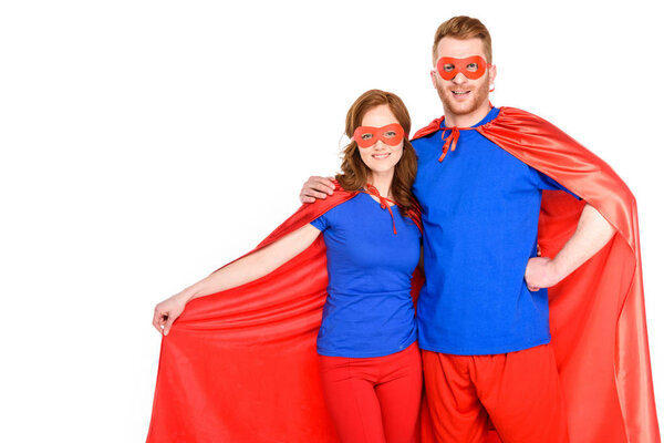 happy couple of superheroes standing together and smiling at camera isolated on white