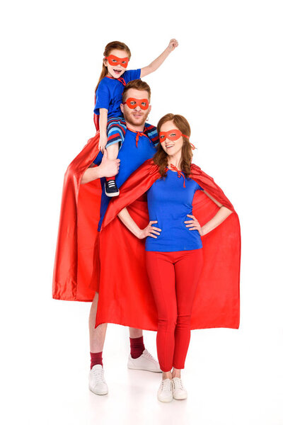 super family with one child in masks and cloaks smiling at camera isolated on white