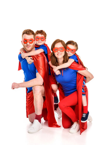 happy super parents piggybacking adorable smiling kids in masks and cloaks isolated on white