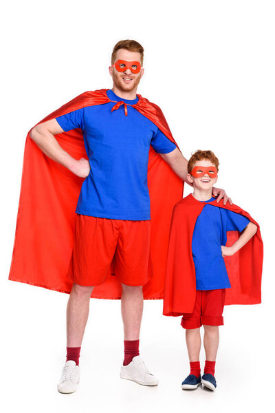 father and son in superhero costumes standing together and smiling at camera isolated on white