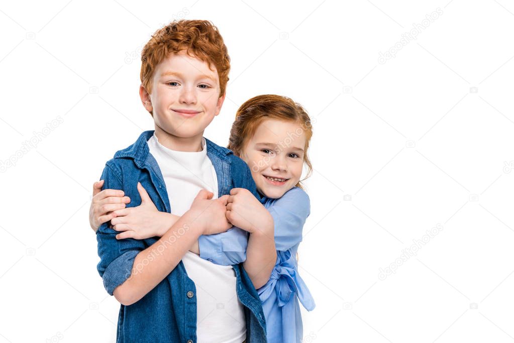 adorable redhead siblings hugging and smiling at camera isolated on white