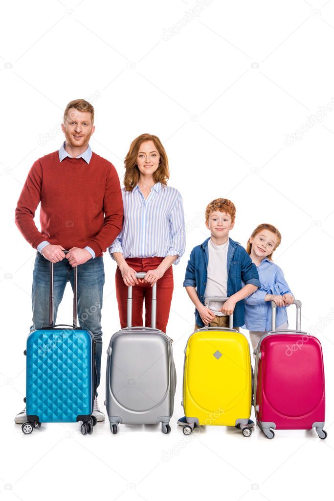 happy redhead family standing with colorful suitcases and smiling at camera isolated on white