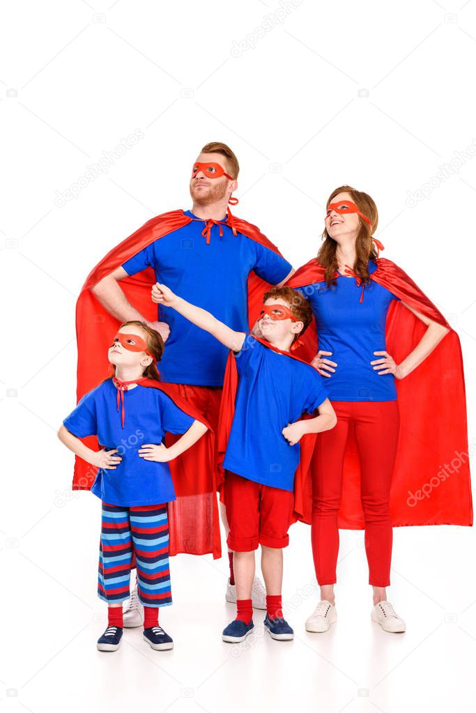 confident family of superheroes in masks and cloaks standing with hands on waist and looking away isolated on white