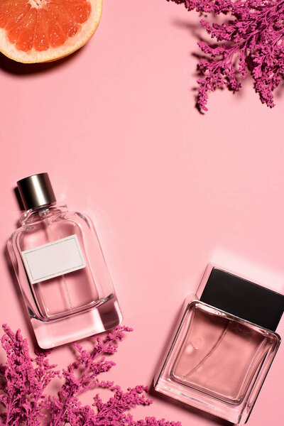 top view of bottles of perfumes with pink flowers and orange on pink surface