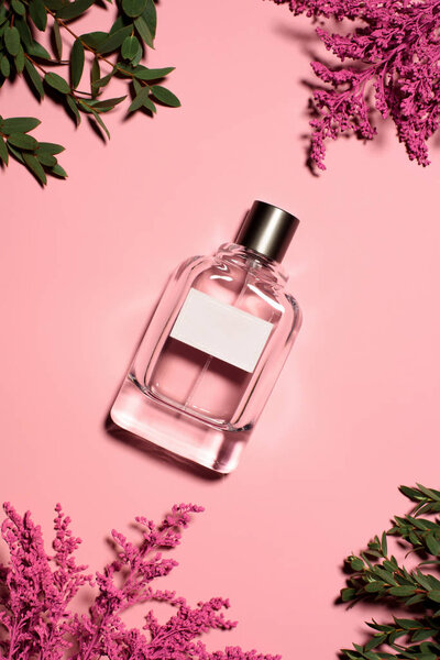 top view of bottle of perfume with flowers and leaves on pink surface