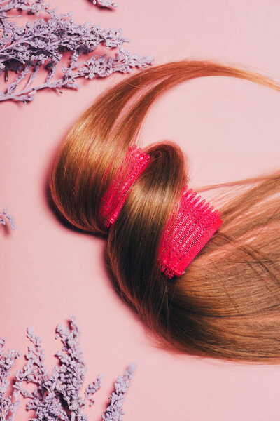 top view of hair rolled over curler with flowers on pink surface