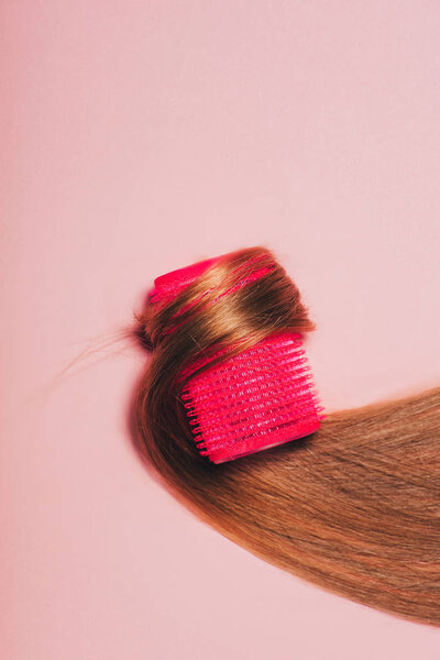 top view of hair rolled over curler on pink surface