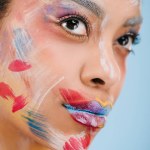Nahaufnahme Porträt einer attraktiven jungen Frau mit Farbstrichen im Gesicht isoliert auf blauem Grund