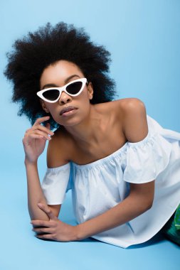 şık giysiler ve güneş gözlüğü mavi katta yatan genç Afro-Amerikan kadın